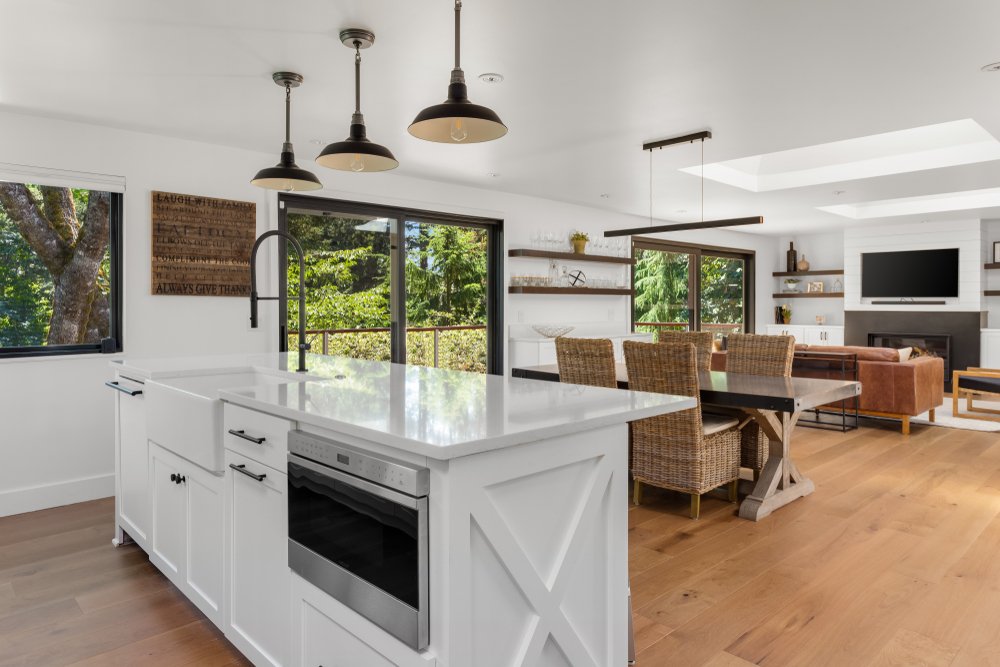 White and Bright Kitchen, Dining, and Living Room in New Luxury Home with Open Concept Floor Plan. Kitchen Features Island with Microwave and Farmhouse Sink.
